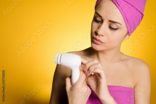 a young girl holding an electric brush for deep cleansing of the skin on her face, looking interested