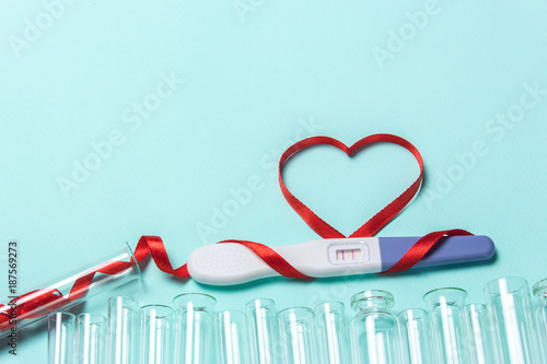 Artificial insemination, a child from a test tube, infertility treatment. Positive pregnancy test with two strips and a red ribbon in the form of a heart and a test-tube photo