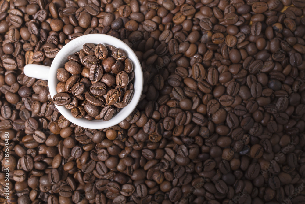 Fototapeta premium Brown coffee beans background with a full white espresso coffee cup