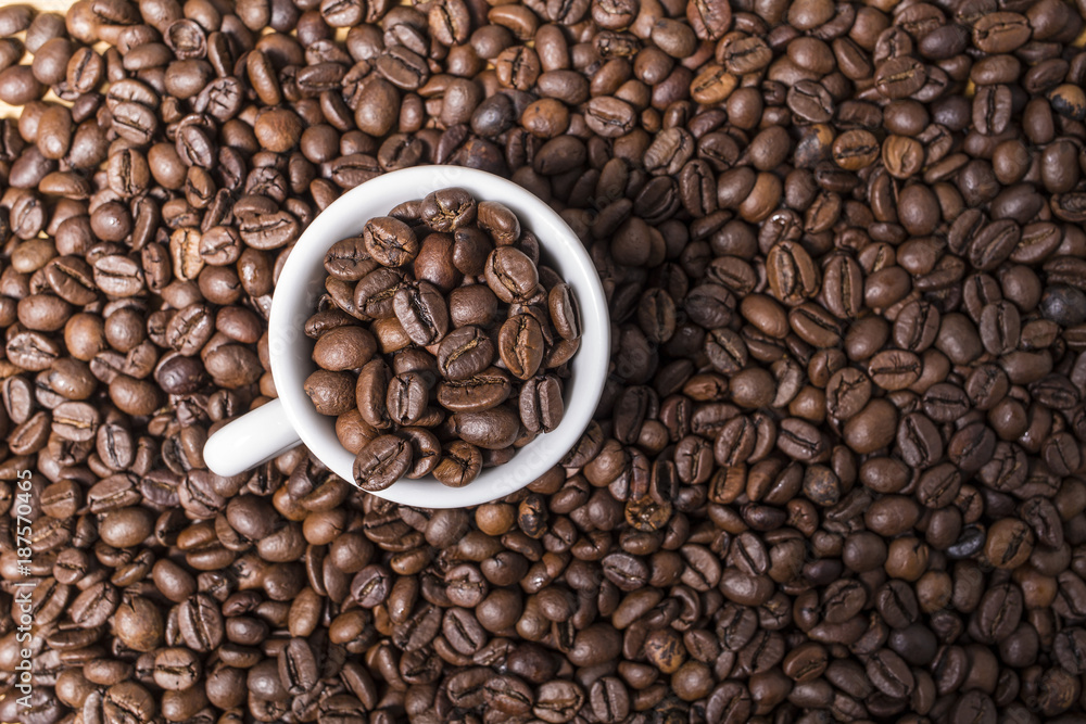 Fototapeta premium White coffee cup with roast coffee beans on a brown coffee grains background