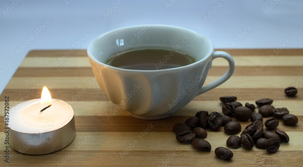 a cup of coffee, coffee beans, a lighted candle a cup of coffee, coffee beans, a lighted candle
