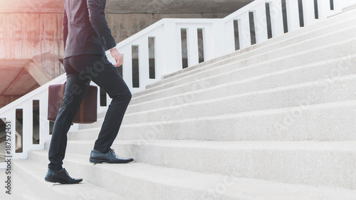 Photos Young Smart Businessman holding suitcase and walking up the stairs