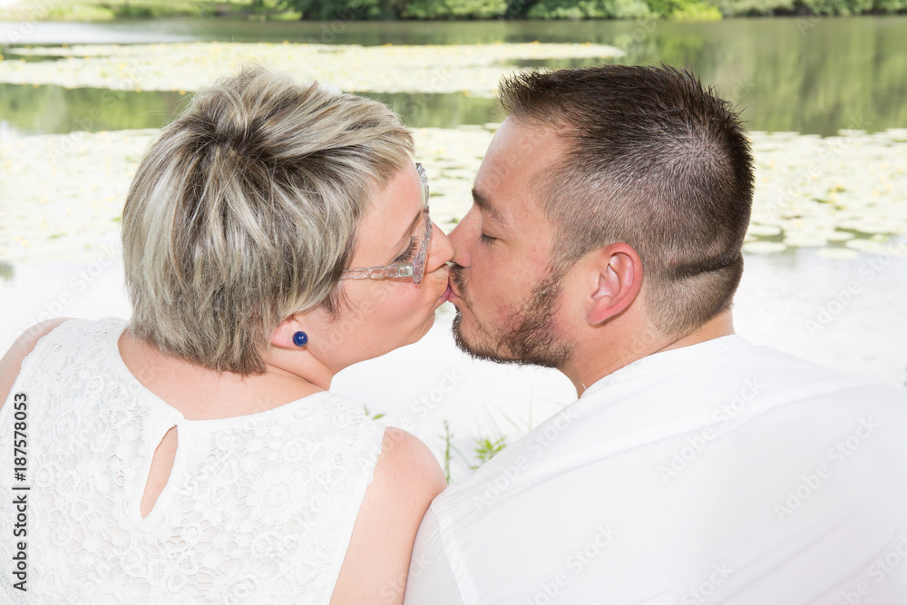 Portrait of young beautiful couple kissing in park with lake Portrait of young beautiful couple kissing in park with lake