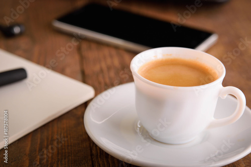  Laptop (notebook) mobile phone (smartphone) and notepad with pen on old wooden table. Work place modern.Cup of coffee