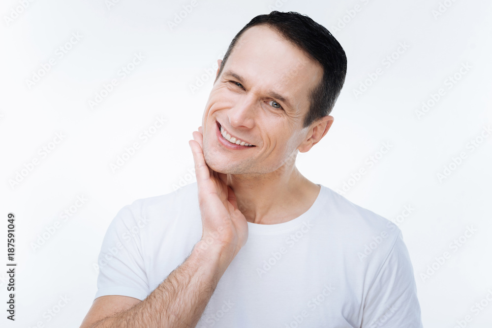 Nice look. Happy delighted man turning his head and touching his chin while looking at you Nice look. Happy delighted man turning his head and touching his chin while looking at you