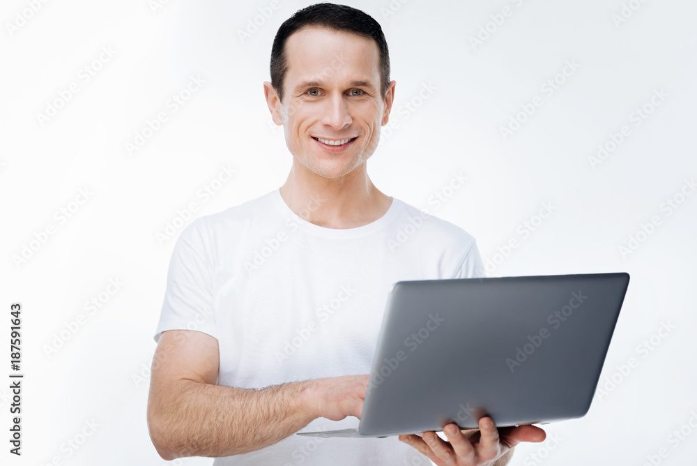 Modern device. Delighted happy nice man smiling and using a laptop while standing against white background Modern device. Delighted happy nice man smiling and using a laptop while standing against white background
