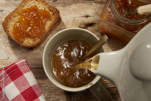 versando il the caldo in una tazza con fette biscottate e marmellata photo