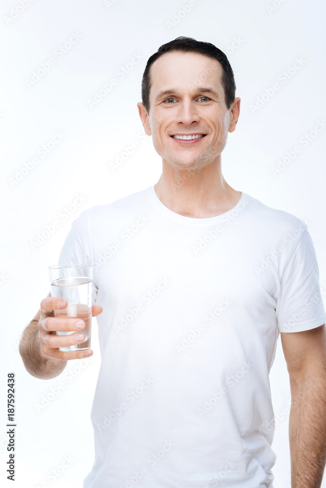 Healthy drink. Joyful nice positive man holding a glass of water and smiling while standing against white background Healthy drink. Joyful nice positive man holding a glass of water and smiling while standing against white background