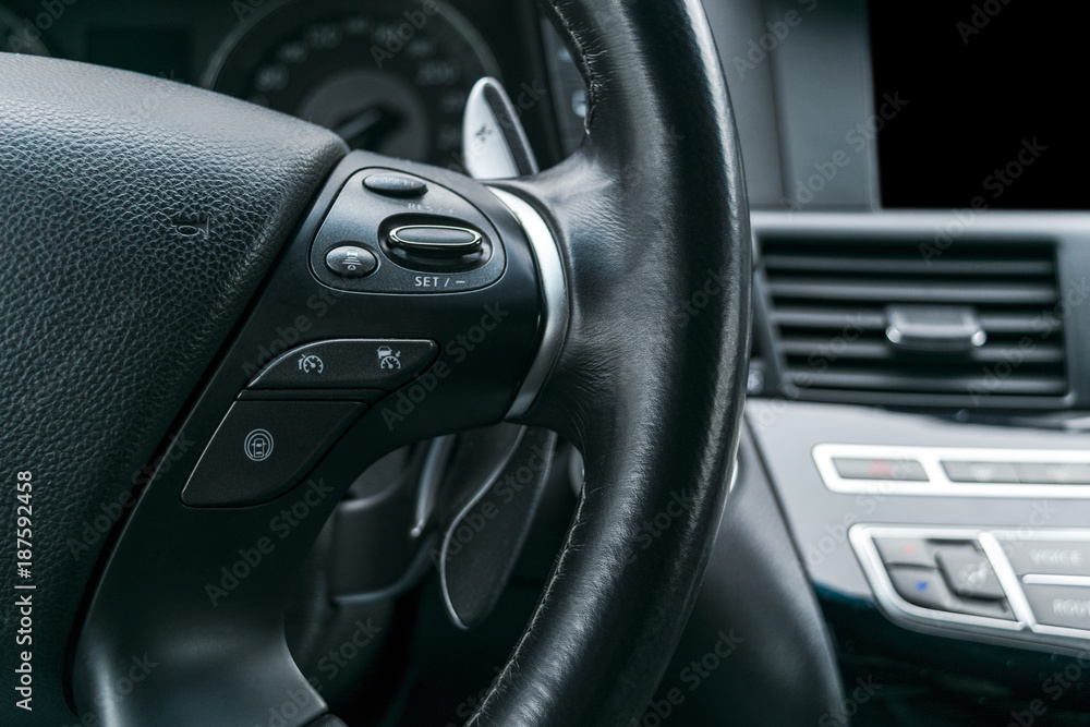 Cruise control buttons on the steering wheel of a modern car with black perforated leather interior. Modern car interior details.