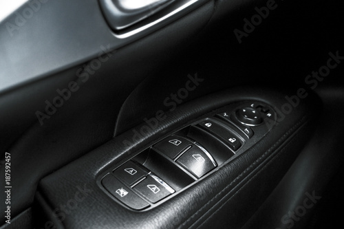 Car black perforated leather interior details of door handle with windows controls and adjustments. Car door handle inside the luxury modern car. Switch button control