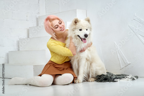 Happy beautiful girl and her big white dog sitting with pleasure in the arms. A beautiful young woman and her pet are best friends. Hug, play and enjoy life.