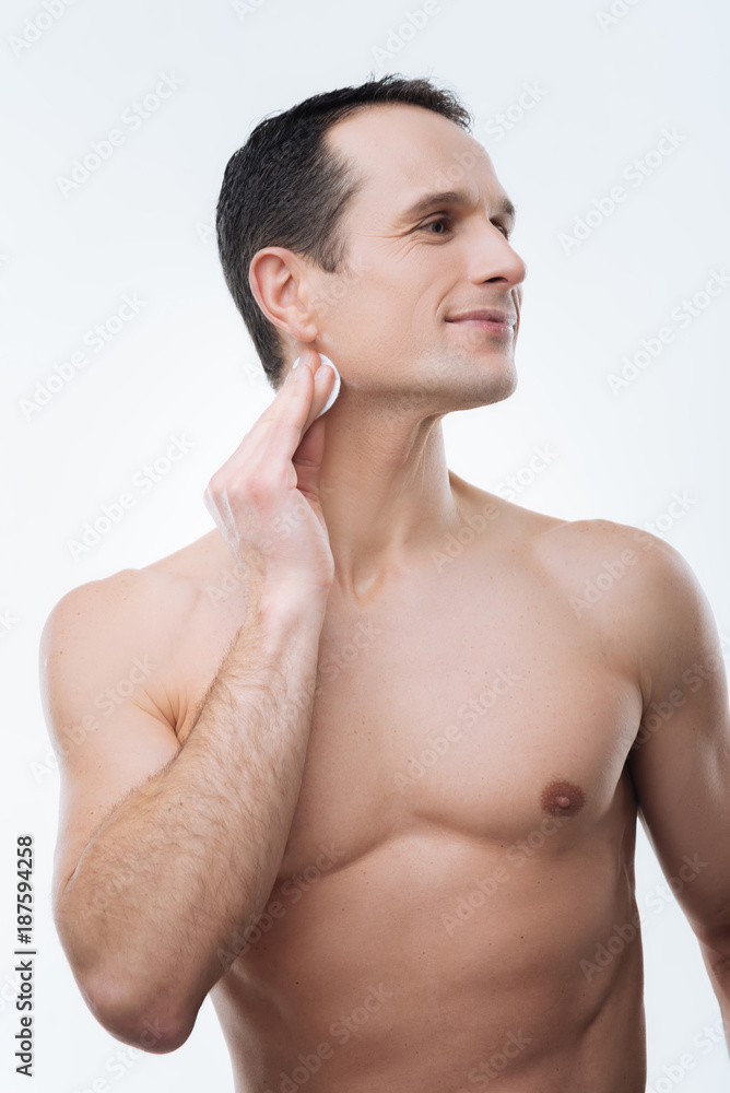 Absolute purity. Pleasant nice delighted man smiling and cleaning his neck while turning his head Absolute purity. Pleasant nice delighted man smiling and cleaning his neck while turning his head