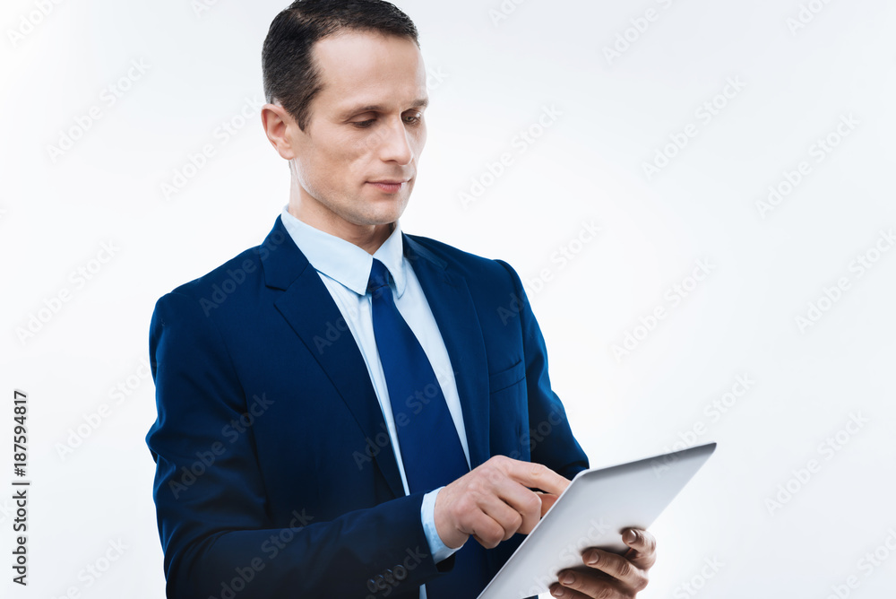 Modern device. Serious nice handsome businessman holding a tablet and using it while working