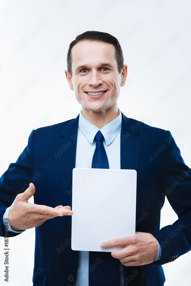 Latest technology. Happy nice delighted businessman pointing at the tablet and smiling while using it for work Latest technology. Happy nice delighted businessman pointing at the tablet and smiling while using it for work