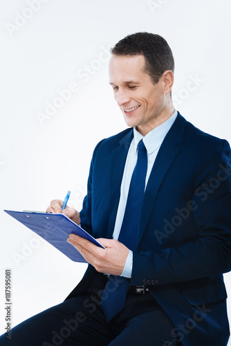 Pleasant job. Delighted joyful successful businessman smiling and taking notes while enjoying his job