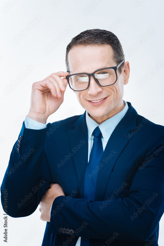 Professional career. Smart nice positive businessman smiling and fixing his eyeglasses while working for a big company Professional career. Smart nice positive businessman smiling and fixing his eyeglasses while working for a big company
