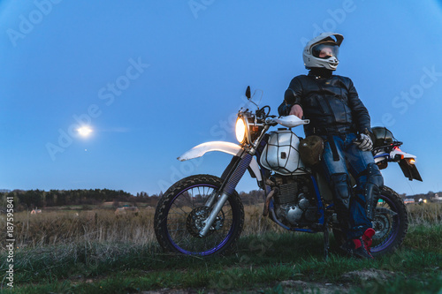 Active way of life, enduro motorcycle, a guy looks at the stars at night and the moon, unity with nature, the spirit of adventure, escape from the hustle and bustle of the city, travel concept
