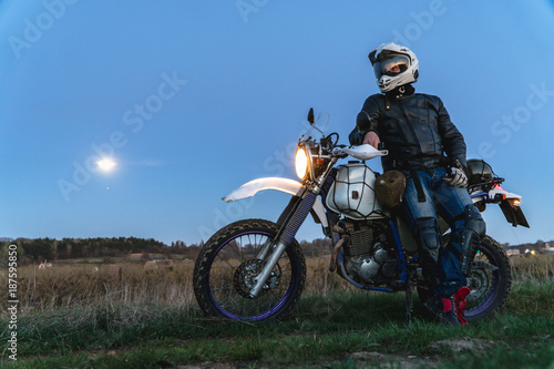 Active way of life, enduro motorcycle, a guy looks at the stars at night and the moon, unity with nature, the spirit of adventure, escape from the hustle and bustle of the city, travel concept