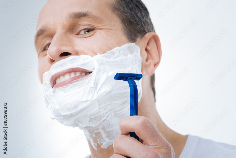 Smooth shaving. Close up of a male razor being in hands of a positive delighted man while shaving