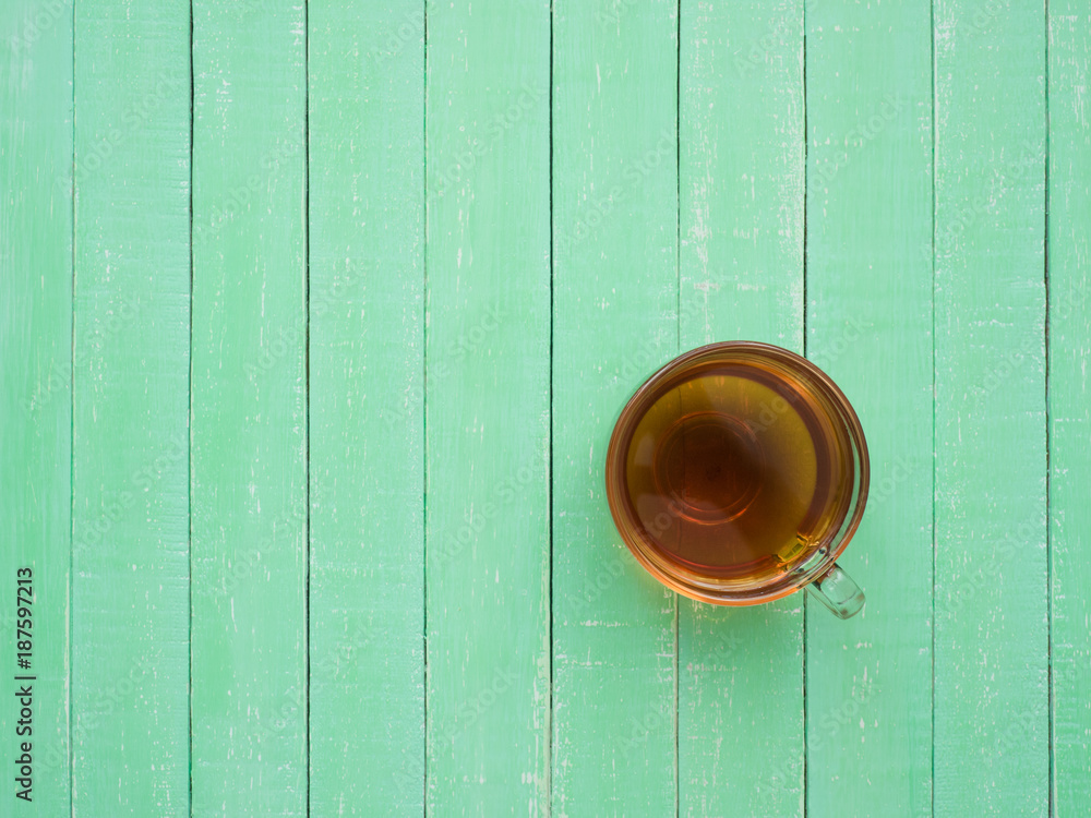 A glass cup of black tea on a mint-colored wooden table A glass cup of black tea on a mint-colored wooden table