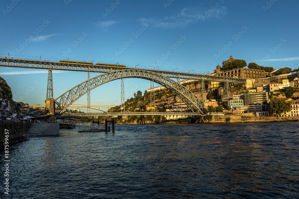 View of the Dom Luis bridge from the bank of the Douro River in Porto, Portugal, during a summer afternoon.