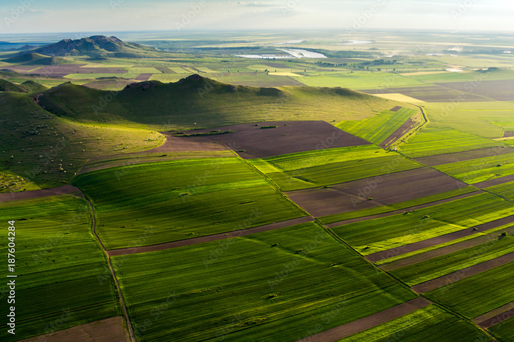 Aerial view over a beautiful scene with green fields, lakes and mountains at golden hour in the spring, Dobrogea , Romania