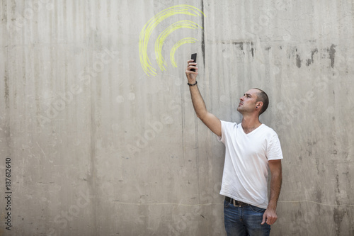 Man holding up phone looking for signal with wifi sign drawn in yellow chalk on concrete wall