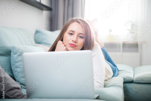 Woman at home using laptop computer on sofa and resting