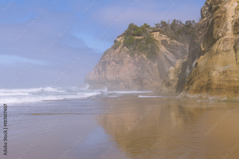 Crashing waves on empty beach with cliffs in fog during sunny day on Hug Point, Oregon, USA