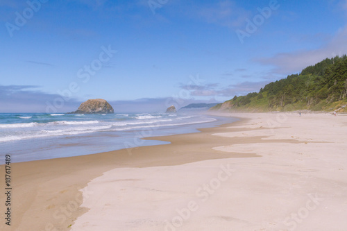 Crashing waves on empty beach with cliffs in fog during sunny day on Hug Point, Oregon, USA