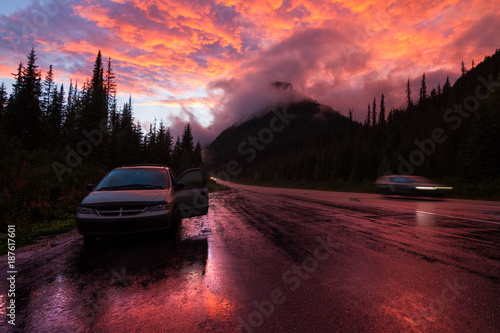 Car on highway with reflections  in Canada surrounded by mountains in clouds during orange sunset © Martin Hossa