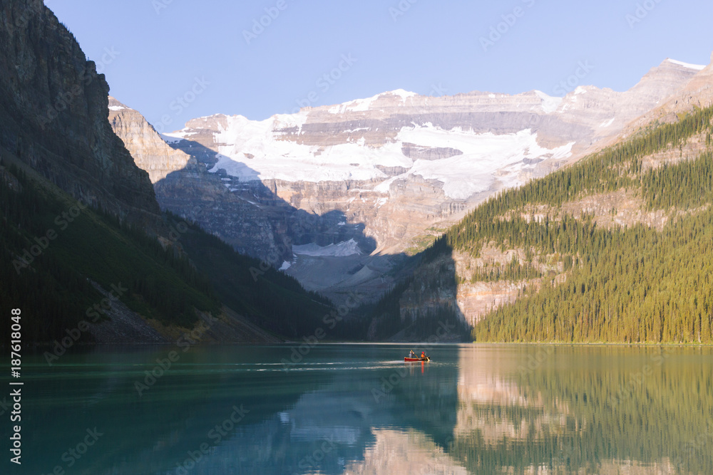 Fototapeta premium People on canoe on Lake Louise with reflection on water in Rocky Mountains in Canada during sunrise on sunny day