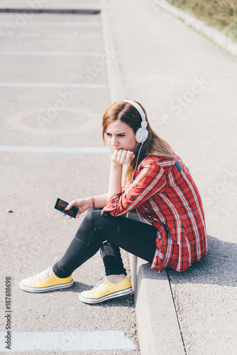 Young woman outdoor in the city listening music with headphones and smartphone hand hold - music, relaxing, technology concept