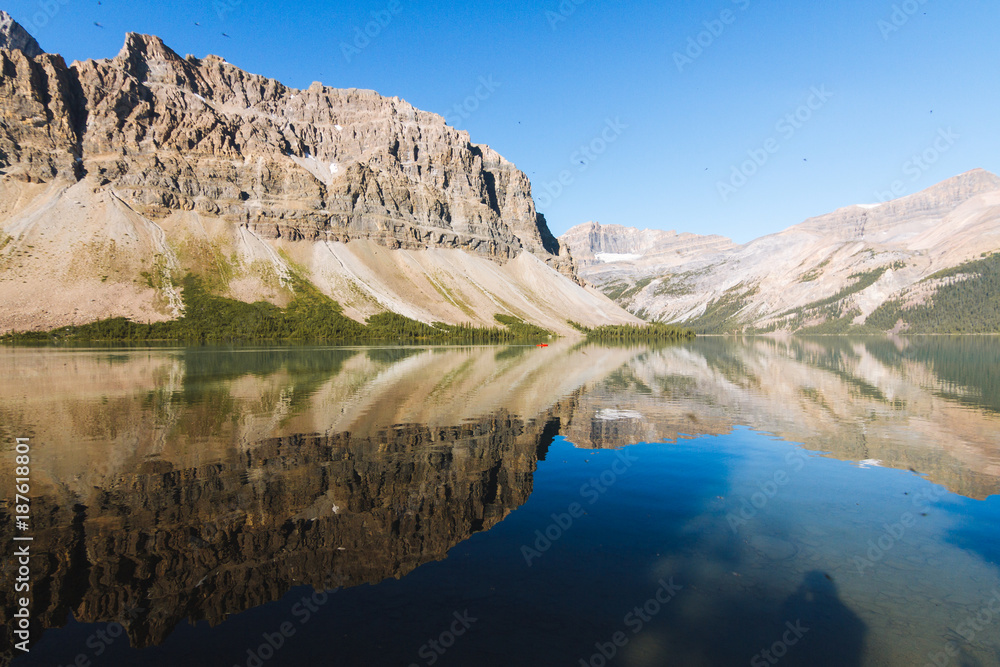 People on canoe on Bow Lake with reflection on water in Rocky Mountains, Alberta during sunrise on sunny day