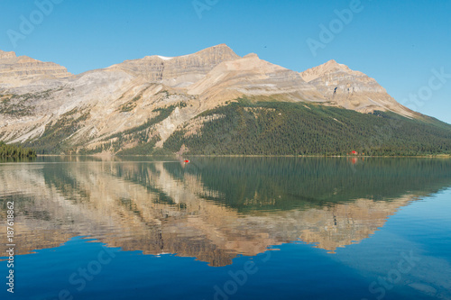 People on canoe on Bow Lake with reflection on water in Rocky Mountains, Alberta during sunrise on sunny day © Martin Hossa