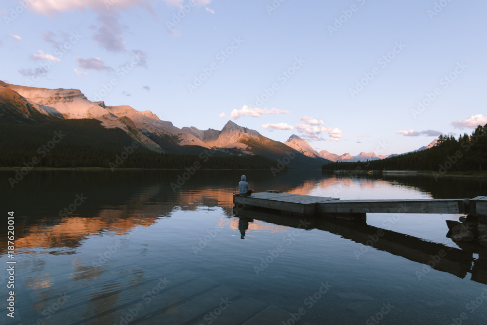 Man sitting on pier on Maligne lake in Rocky Mountains during colorful sunset with clouds