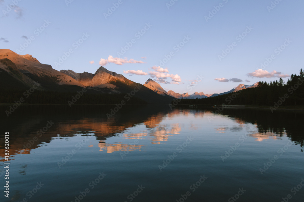 Reflections on Maligne lake in Rocky Mountains during colorful sunset with clouds