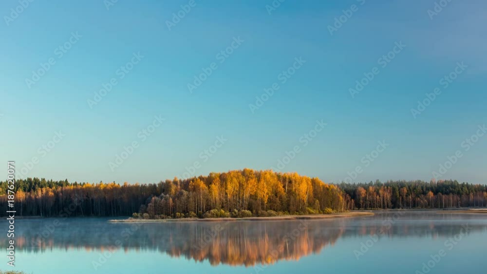 Cold silent morning. Mist rises from the water. Autumn landscape of a forest in beautiful fall colors reflected in the waters of a lake. Zoom in timelapse. Cold silent morning. Mist rises from the water. Autumn landscape of a forest in beautiful fall colors reflected in the waters of a lake. Zoom in timelapse.