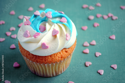Cupcake for valentine's day with whipped cream and pink confectionery sprinkling In the form of hearts on blue background. Picture for a menu or a confectionery catalog.