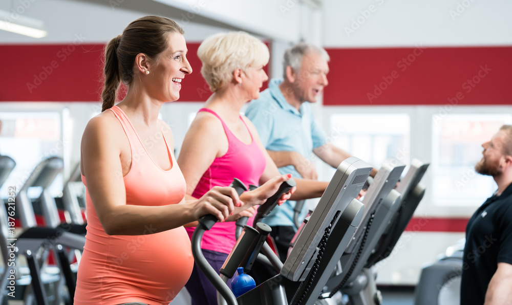 Pregnant woman and seniors training on cross trainer at the gym