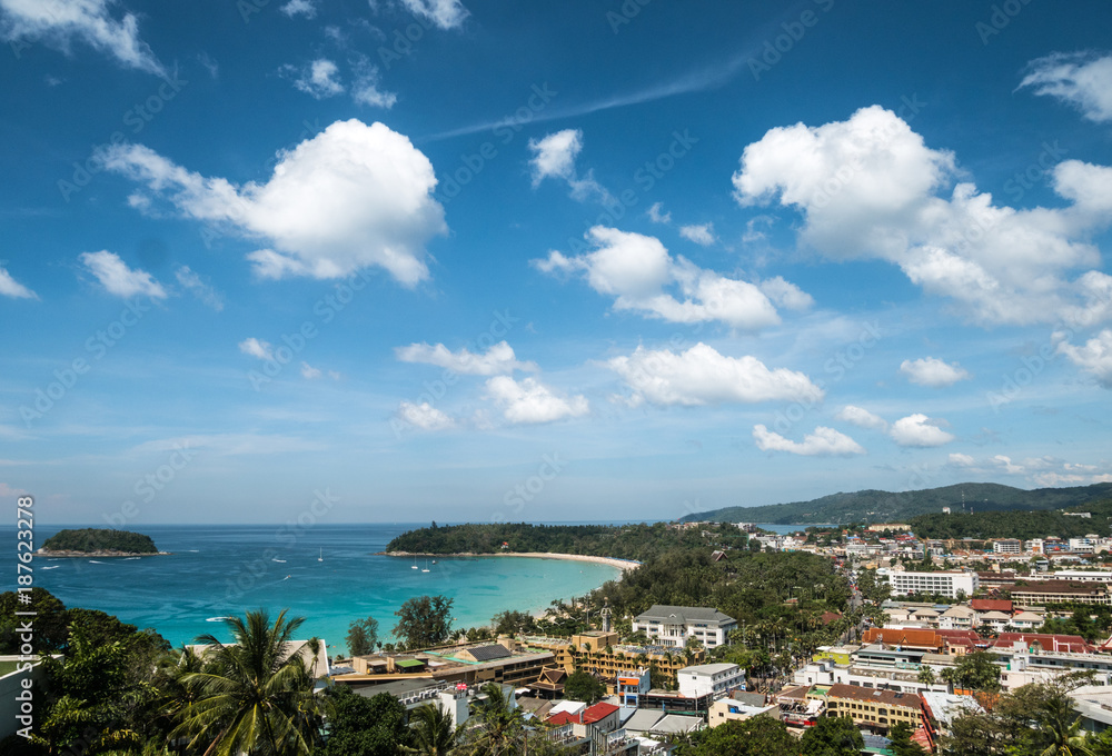 view of kata beach and kata city in phuket with boat traffic on the sea and clouds on bluie sky.