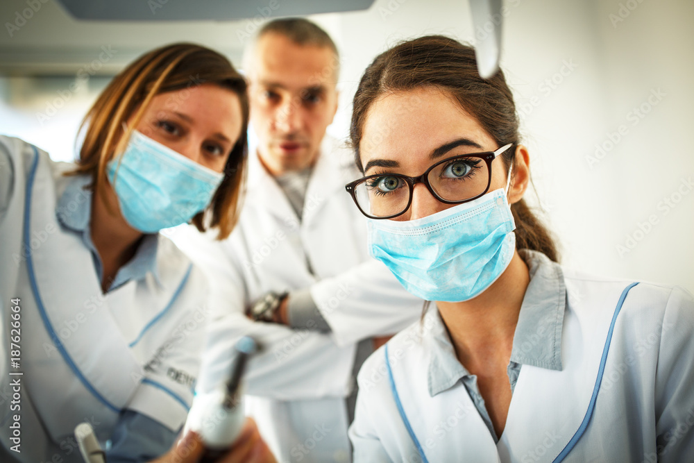 Dentist and her female assistant in dental office examining patient teeth.Camera angle from patients perspective.