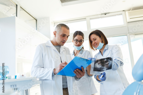 Zespół dentystów medycznych w gabinecie stomatologicznym dyskutuje o praktyce i badaniu listy pacjentów.