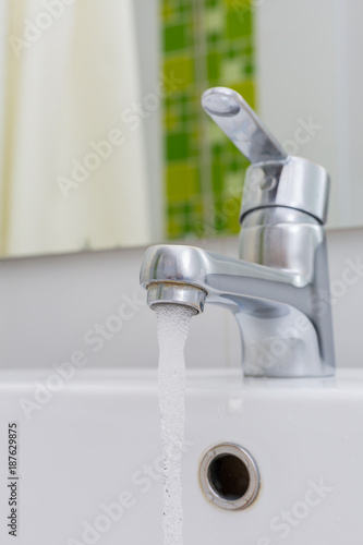 Modern chrome tap faucet with running water.