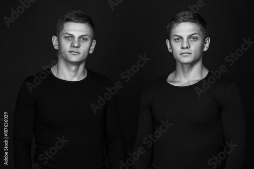 Two attractive positive young twin brothers standing dressed in 