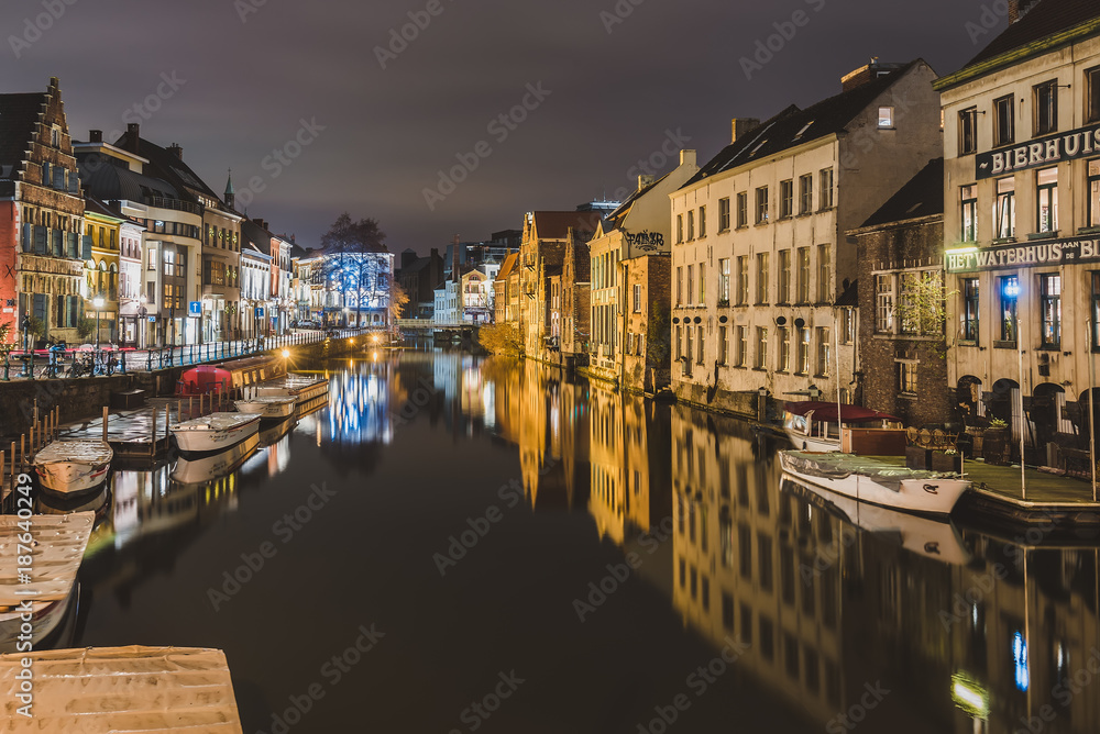 Ghent, Flanders, Belgium - January 3th, 2017. Night Gent Old town embankment with illuminated medieval merchant houses and private boats reflected on the water of canal by evening lights. 