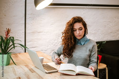 Foto Woman reading book while sitting by the desk.