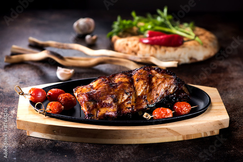 Grilled pork ribs in a frying pan and baked tomatoes
