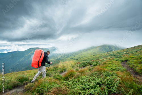 Traveler with trekking sticks and a backpack walks of the mountains in the clouds