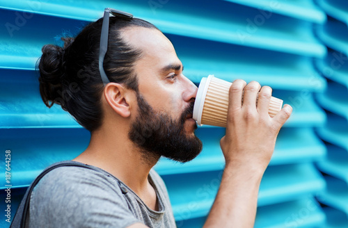 man drinking coffee from paper cup over wall